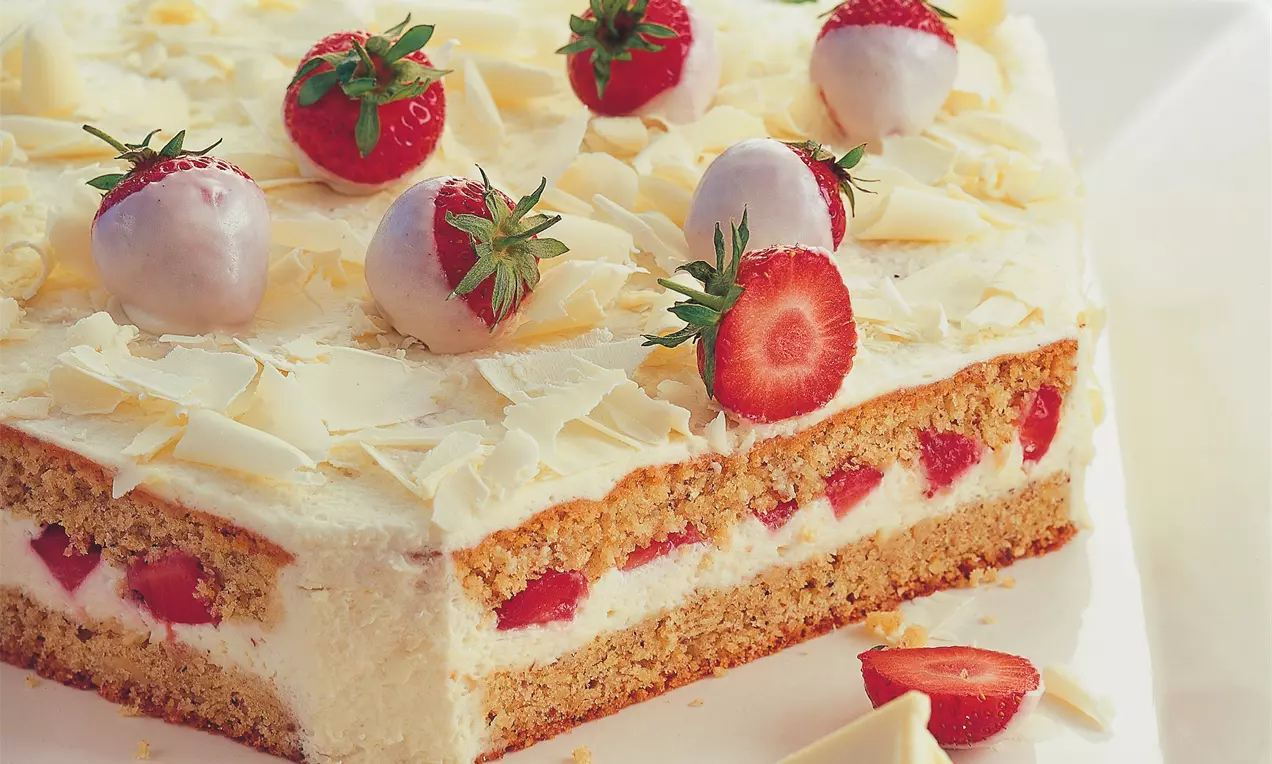Kockasta torta od bijele čokolade s bijelim slojem ukrašena jagodama i strugotinama čokolade na svijetlom tanjiru