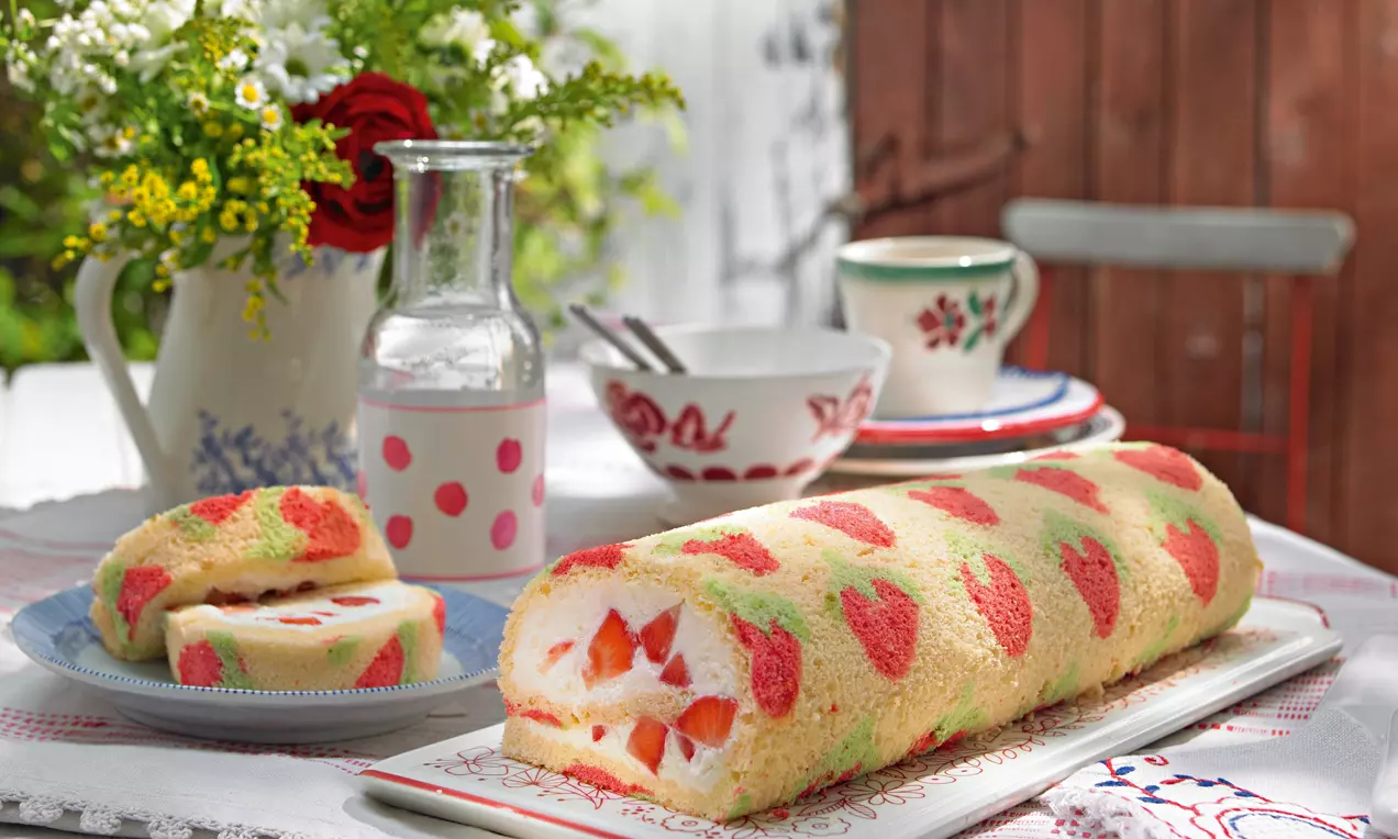 Svijetložuta rolada s motivom crvenih jagoda, spiralno ispunjena bijelom kremom i komadićima jagoda, servirana na bijelom tanjuru