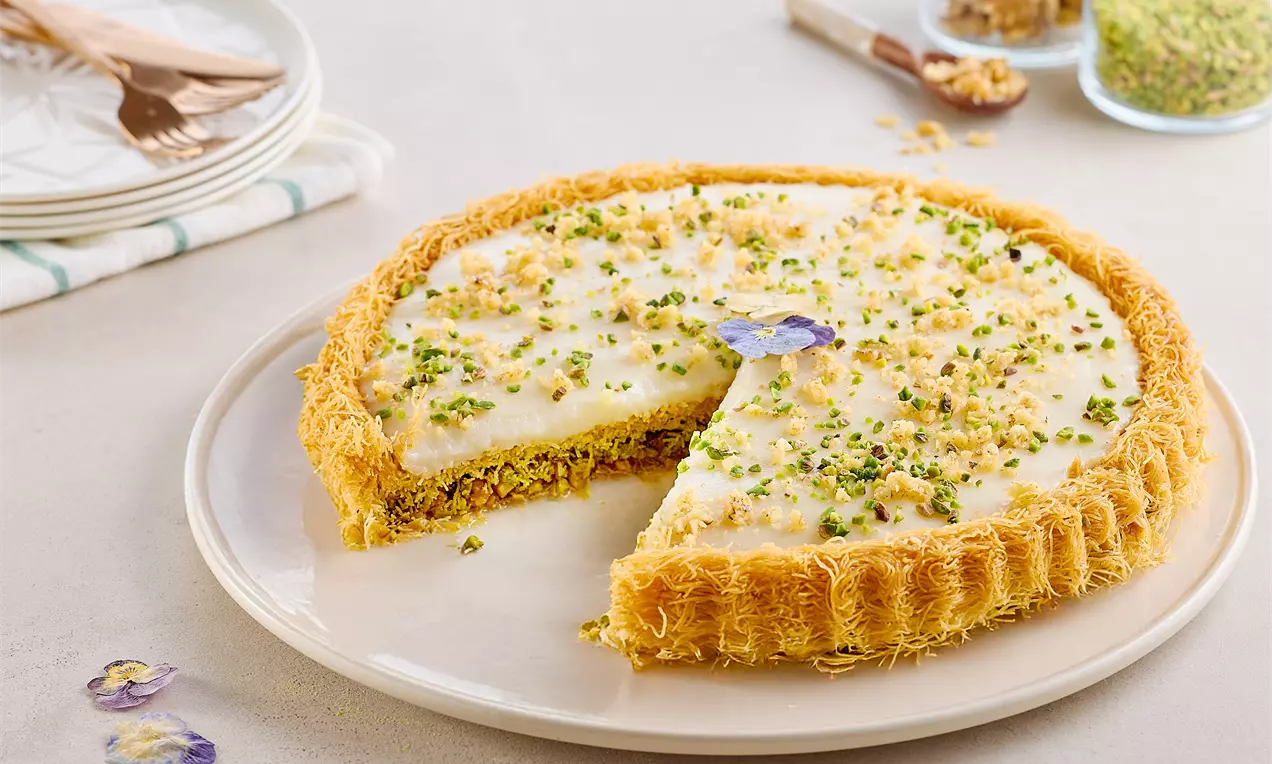 Tart s hrskavim zlatnosmeđim tel kadayif rubom, kremasto bijelim punjenjem, posut usitnjenim pistacijama na svijetlom tanjiru