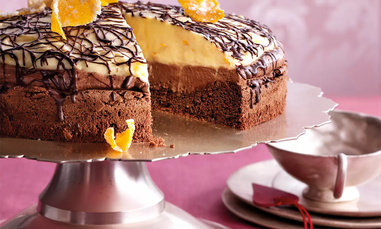 Čokoladno-narančasta torta na srebrnom stalku s kremastim slojevima, preljevom od tamne čokolade i ukrasima od kandirane naranče