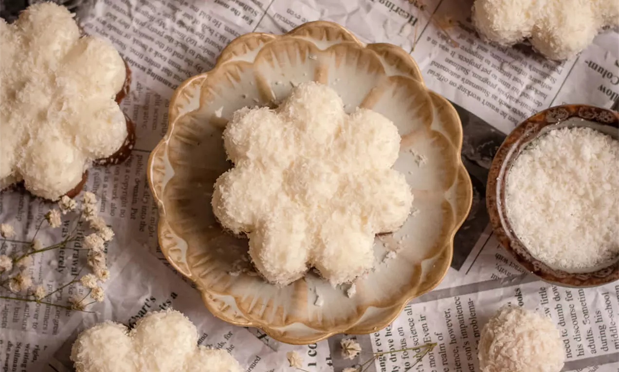 Bijele kokosove cvjetne praline s pahuljastom teksturom uredno složene na tanjir i papirnu podlogu, uz dekorativne grančice i zdjelicu kokosa